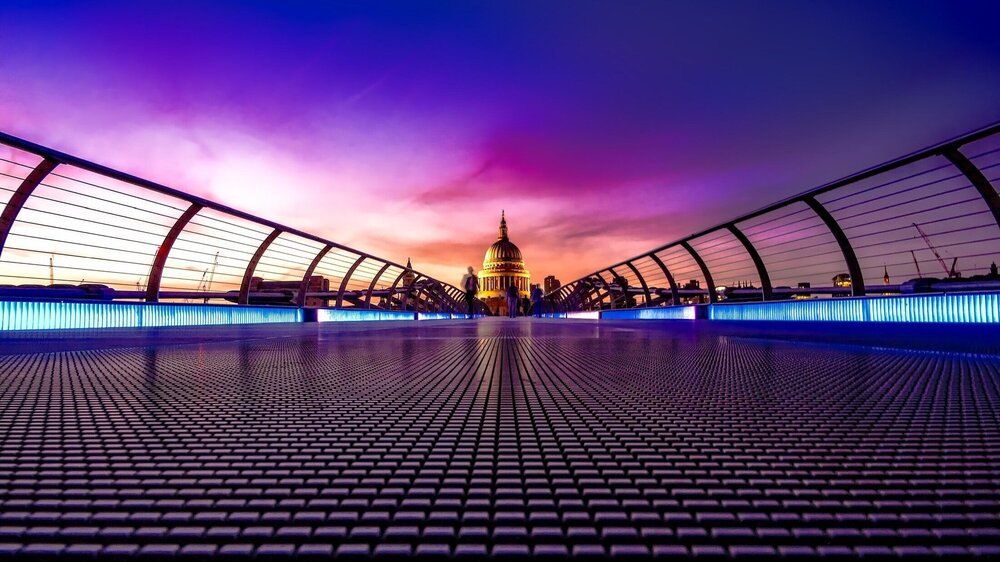 View from the Millennium Bridge at twilight with a vibrant purple and pink sky, leading towards the illuminated dome of St. Paul's Cathedral in London